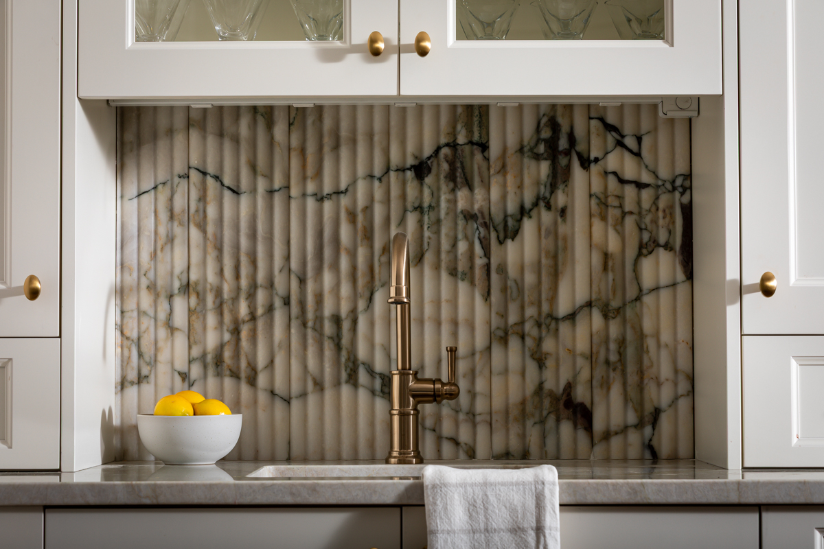 Kitchen backsplash with marble pattern, white cabinets, a bowl of lemons, and a white towel under the faucet.