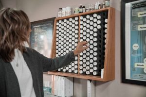 Person reaching into a cabinet filled with small bottles, with a framed chart on the wall nearby.