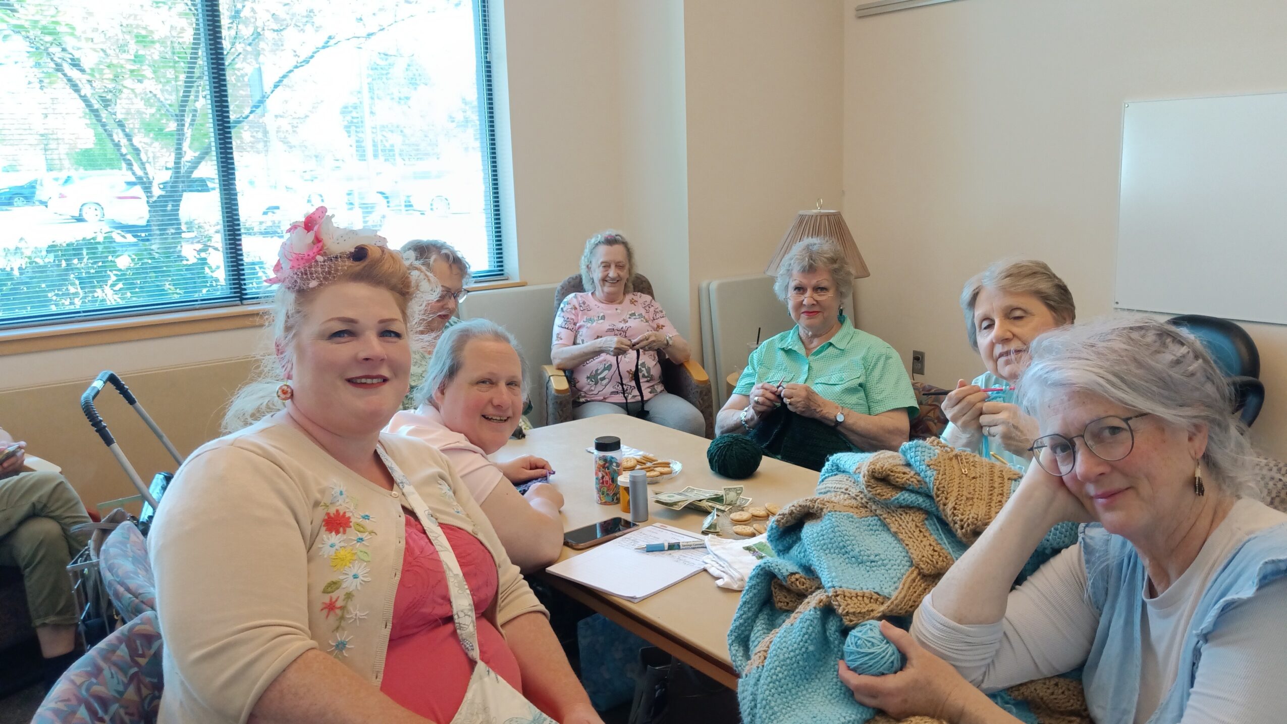Group of women sitting around a table in a room with a window, smiling and engaging in conversation.