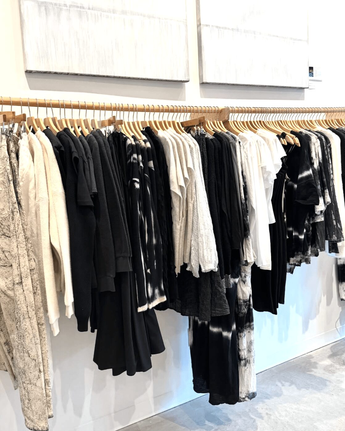 Clothing rack with black, white, and patterned garments hanging on wooden hangers, against a white wall background.