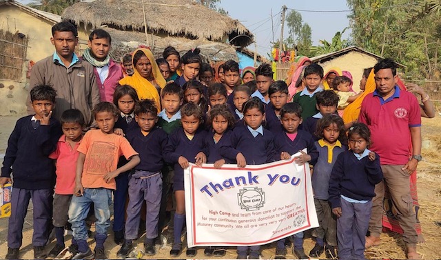 Group of children and two adults holding a thank you banner outdoors in a rural setting.