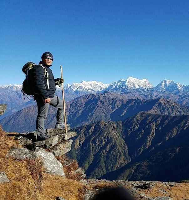 Hiker standing on rocky ledge with mountains and snow-capped peaks in background.