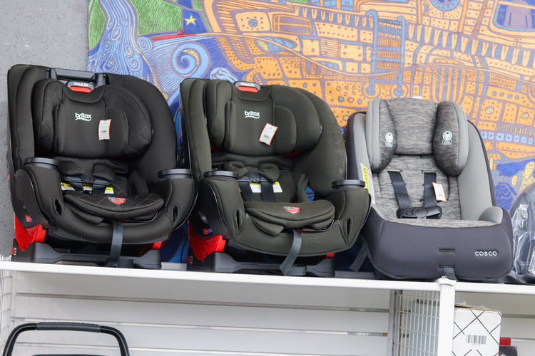 Three car seats on a white shelf, two black and one gray, with a colorful mural in the background.