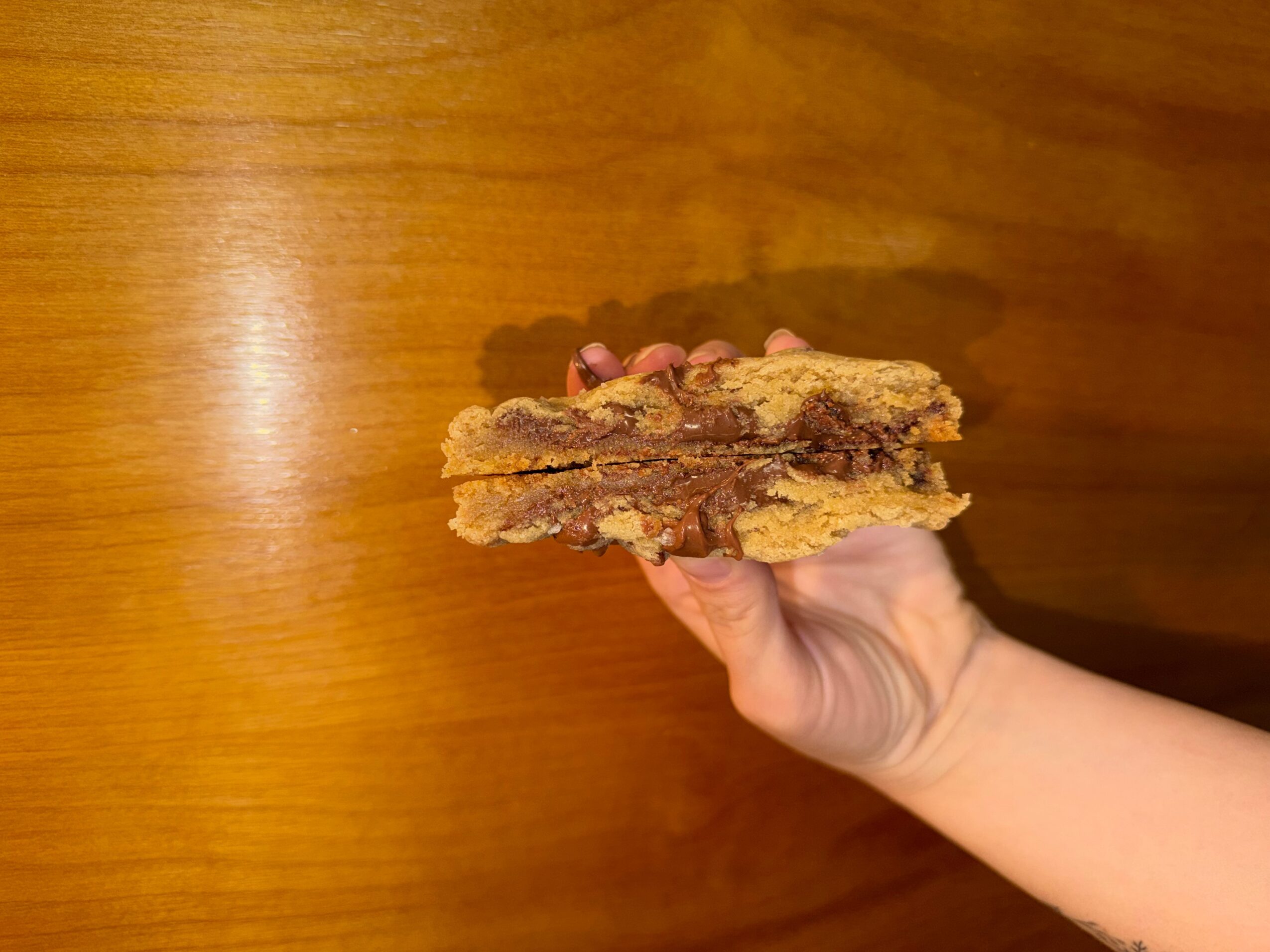 Hand holding a layered cookie or snack bar with a wooden background.