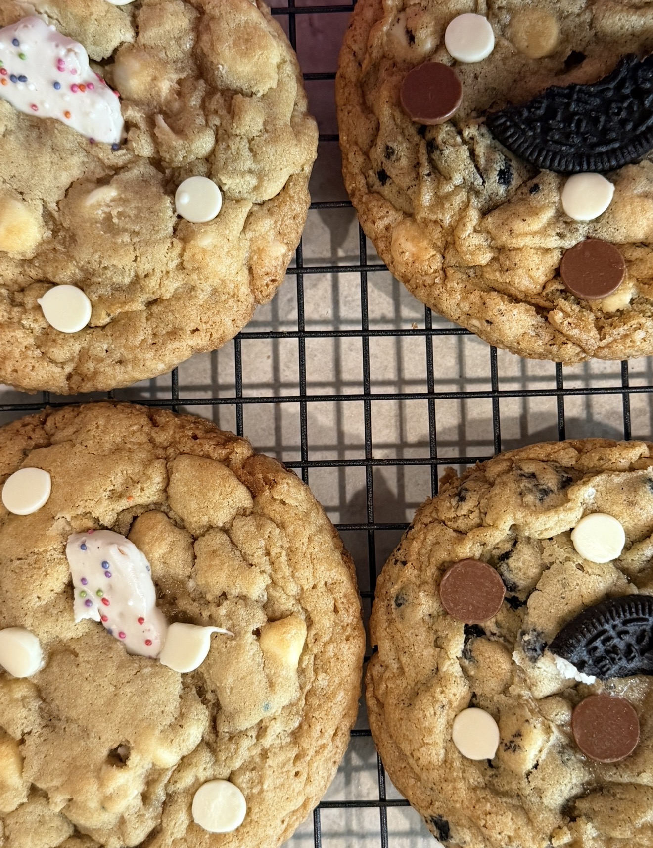 Four large cookies with white, chocolate, and Oreo pieces on a wire cooling rack.