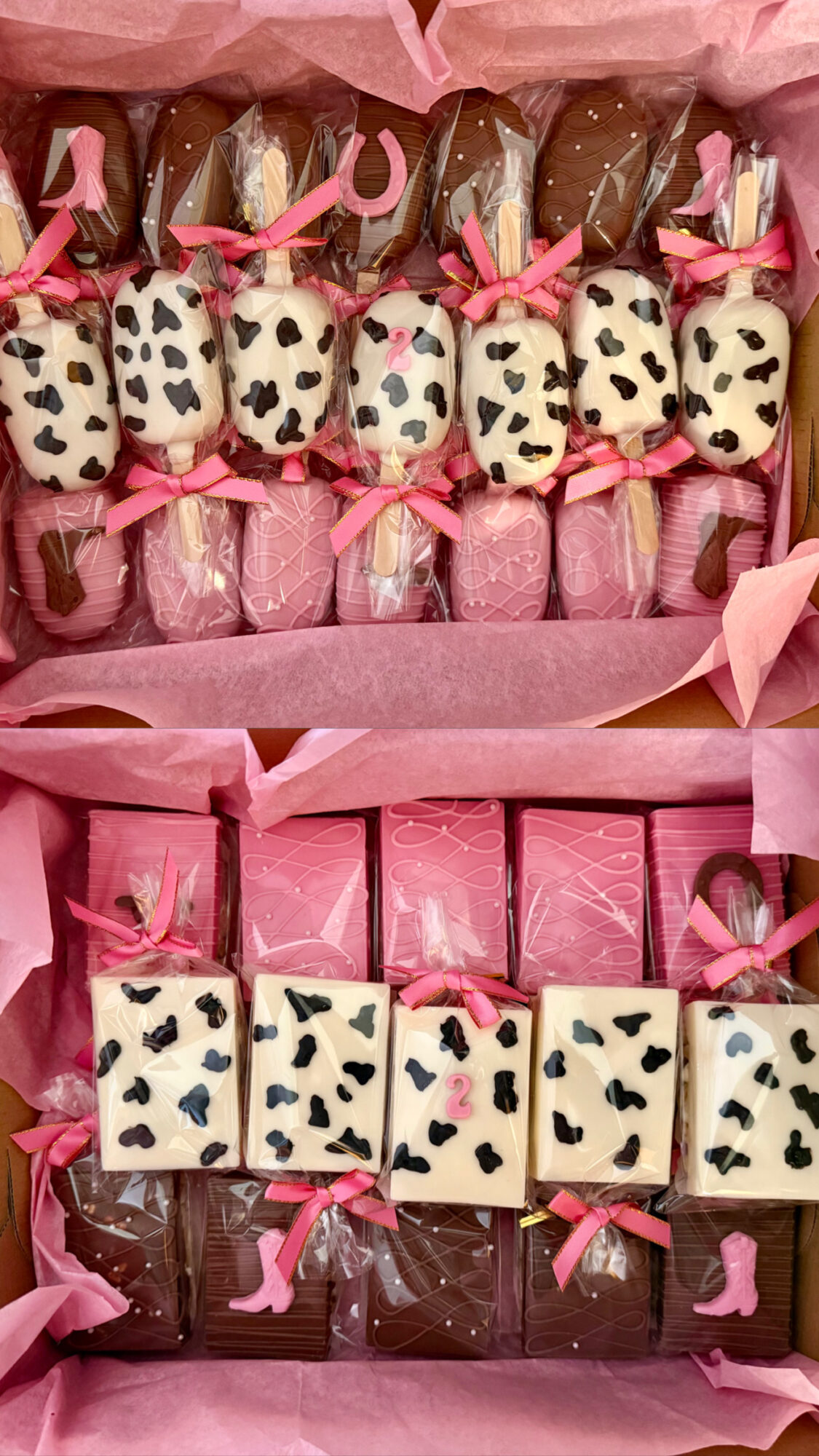 Box of decorated chocolates with pink ribbons, some with leopard print, arranged in rows inside a pink box.