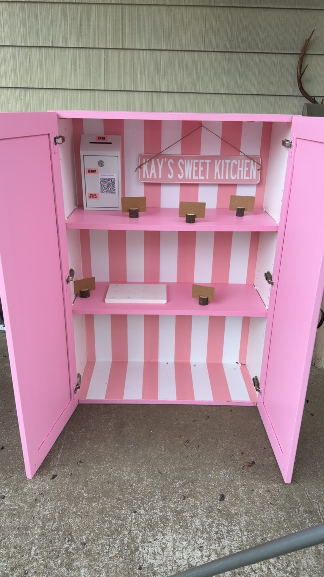 Pink and white striped toy kitchen cabinet with shelves and a sign reading 'MAY'S SWEET KITCHEN'.