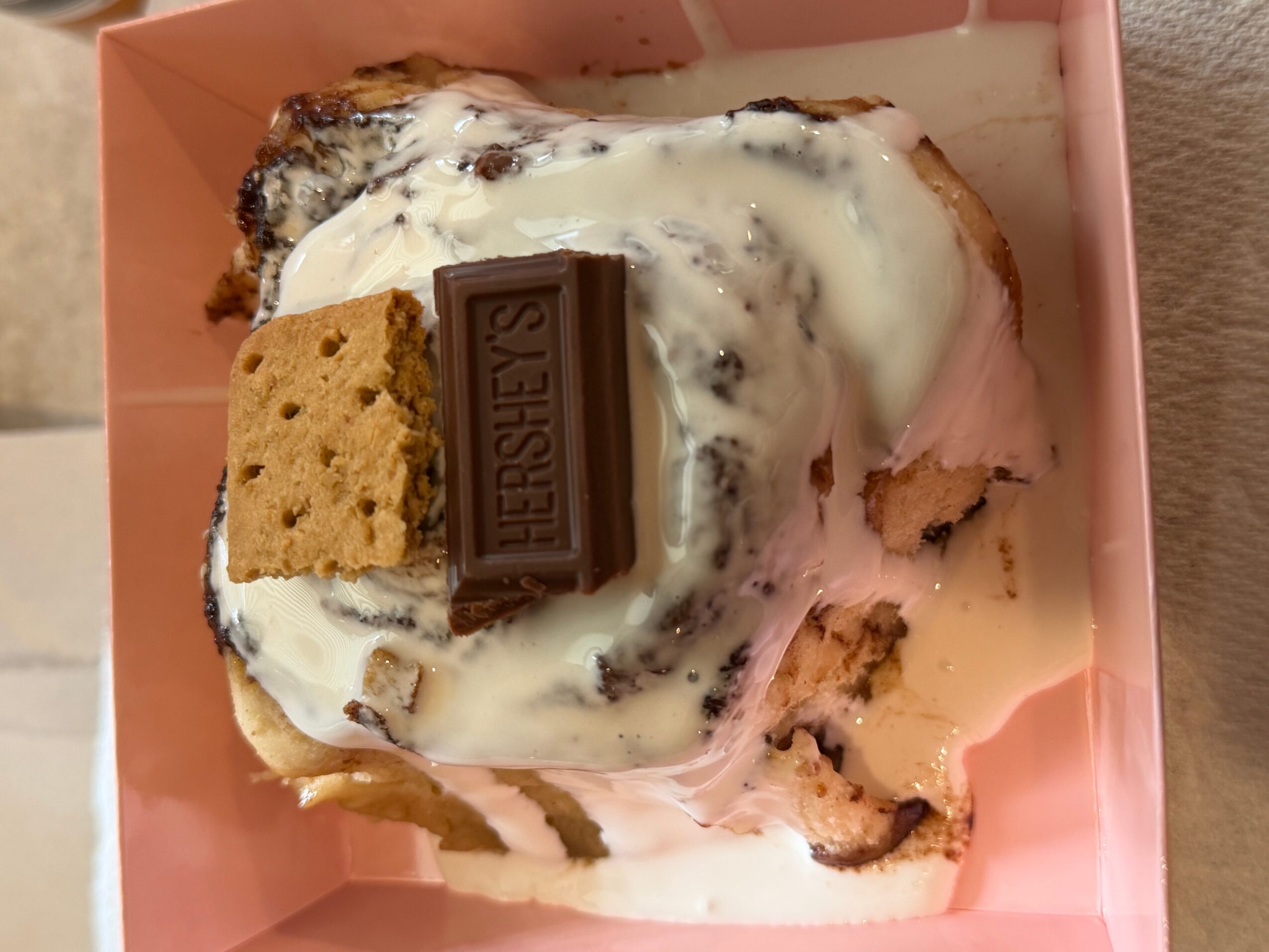 A partially eaten dessert with ice cream, a cookie, and a Hershey's chocolate piece in a pink box.