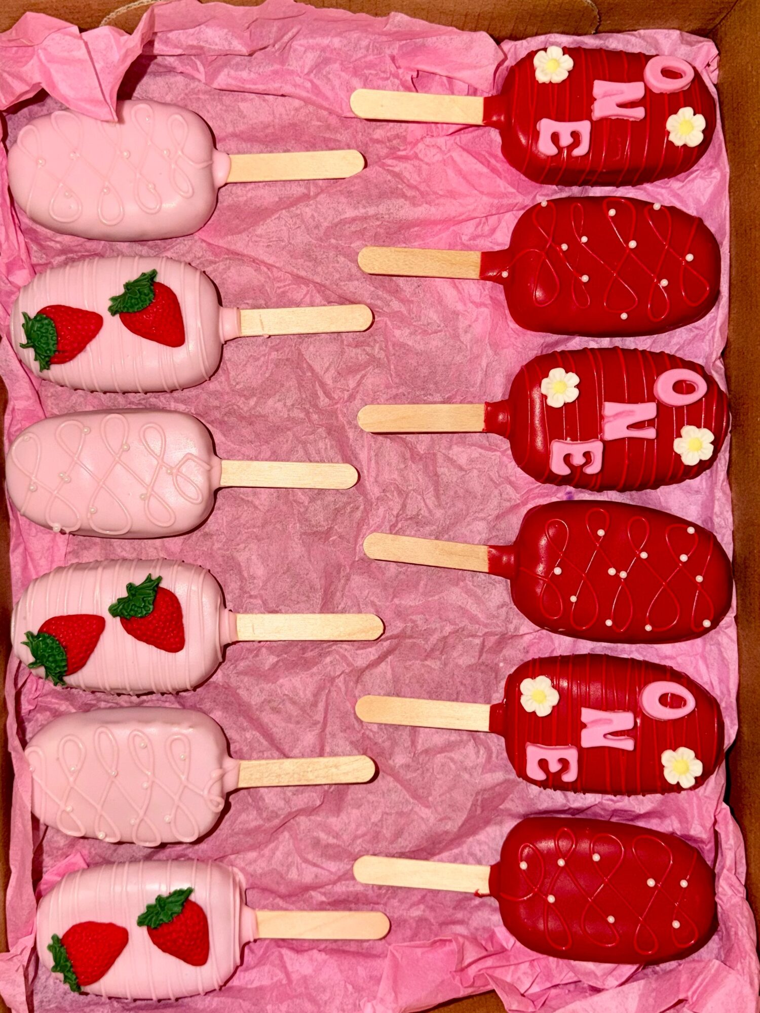Six strawberry and cream popsicles with red, pink, and white colors on pink tissue paper, arranged vertically.