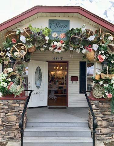 Flower arch with baskets and flowers above entrance, house number 307, open door showing interior, sign reading 'Sleep'.