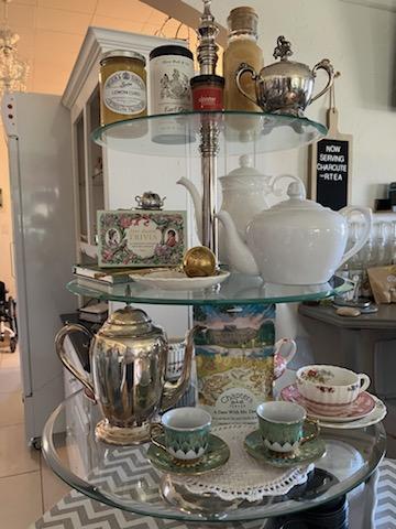 Glass shelf with teapot, cups, jars, and decorative items, displayed on a round table with a chevron-patterned cloth.
