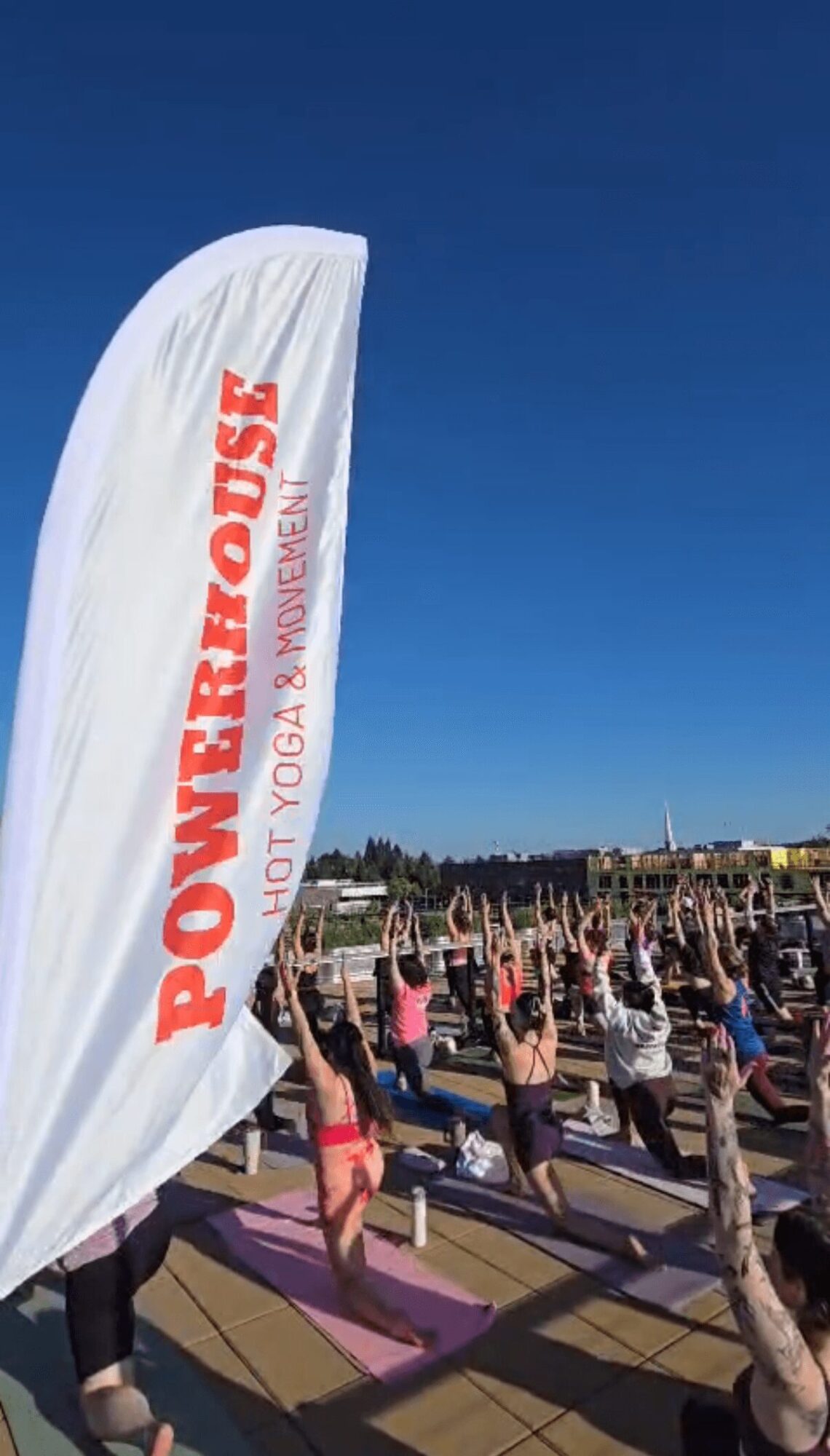 Group of people practicing yoga outdoors on mats, with a large banner reading 'Powerhouse' and a clear blue sky.
