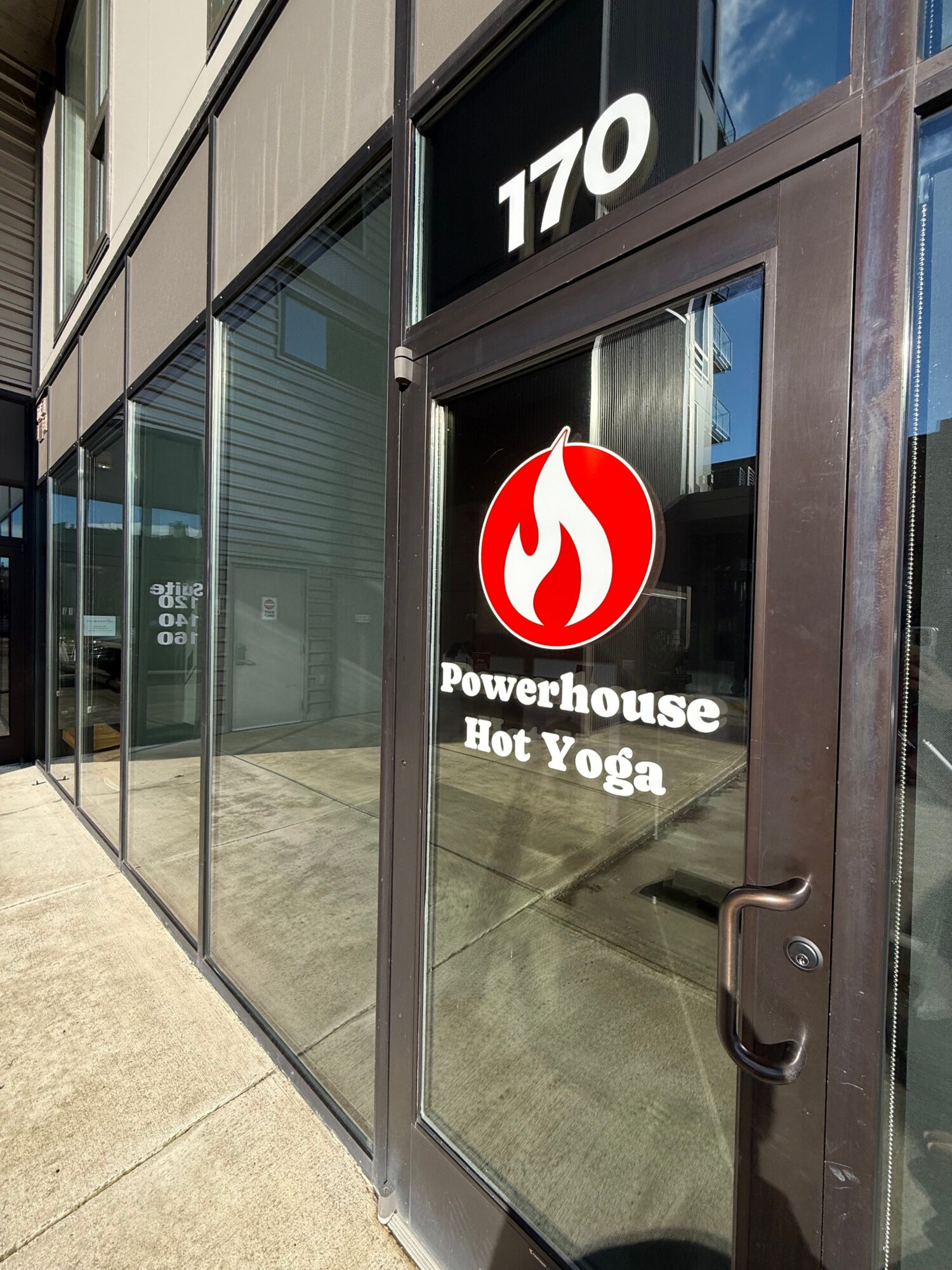 Glass door with Powerhouse Bik Yoga sign and logo, building number 110, sidewalk outside.