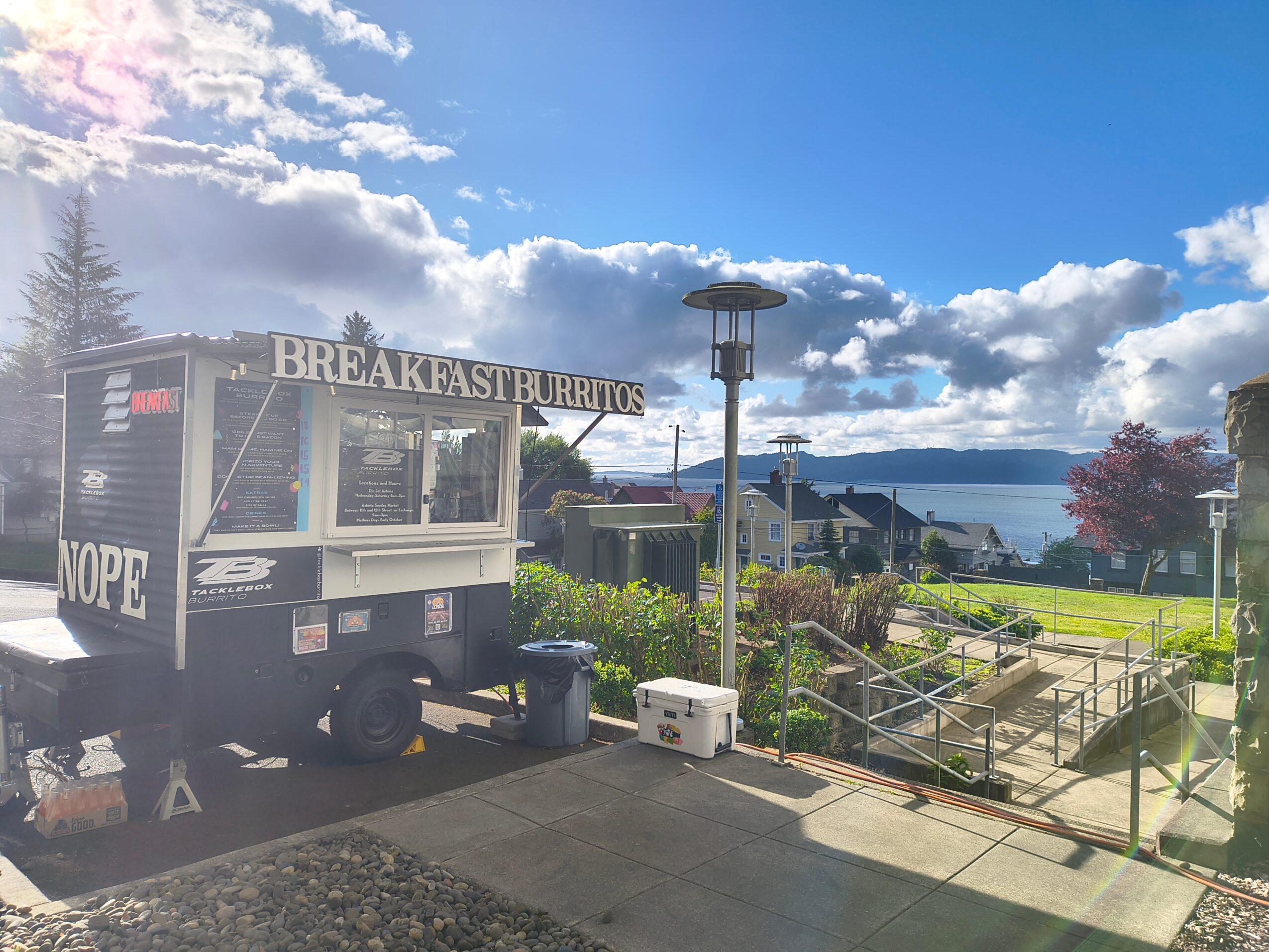 Food cart with a sign reading 'BREAKFAST BURRITOS' and a cloudy sky background.