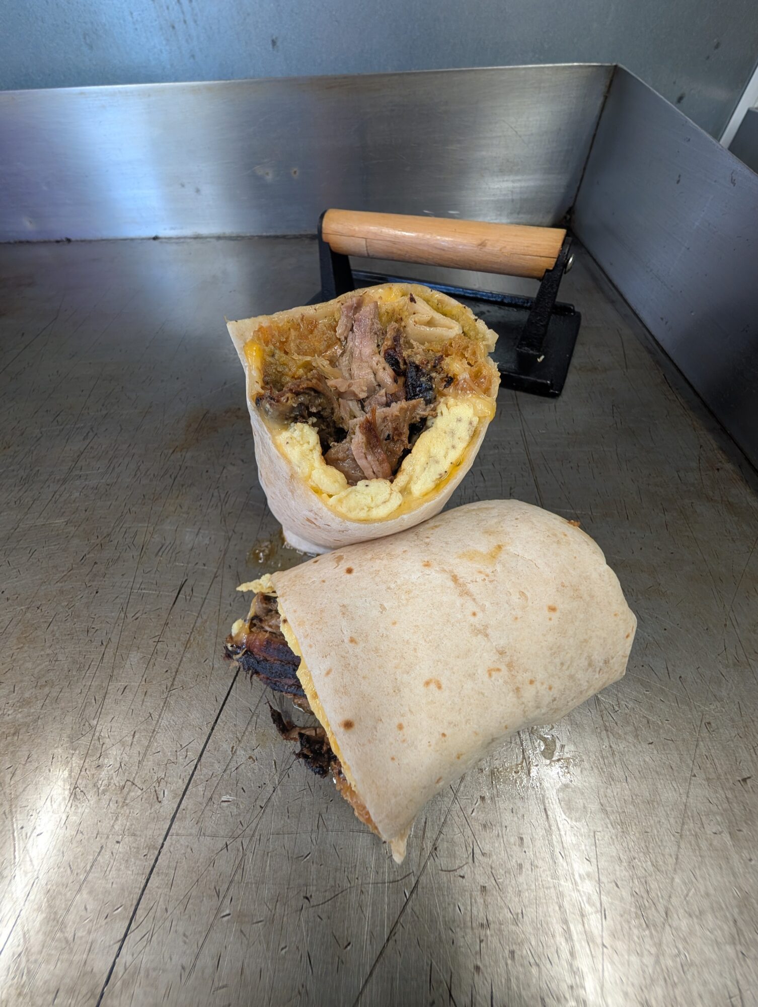 Two burritos on a metal surface, one cut open showing beans and meat, with a rolling pin in the background.