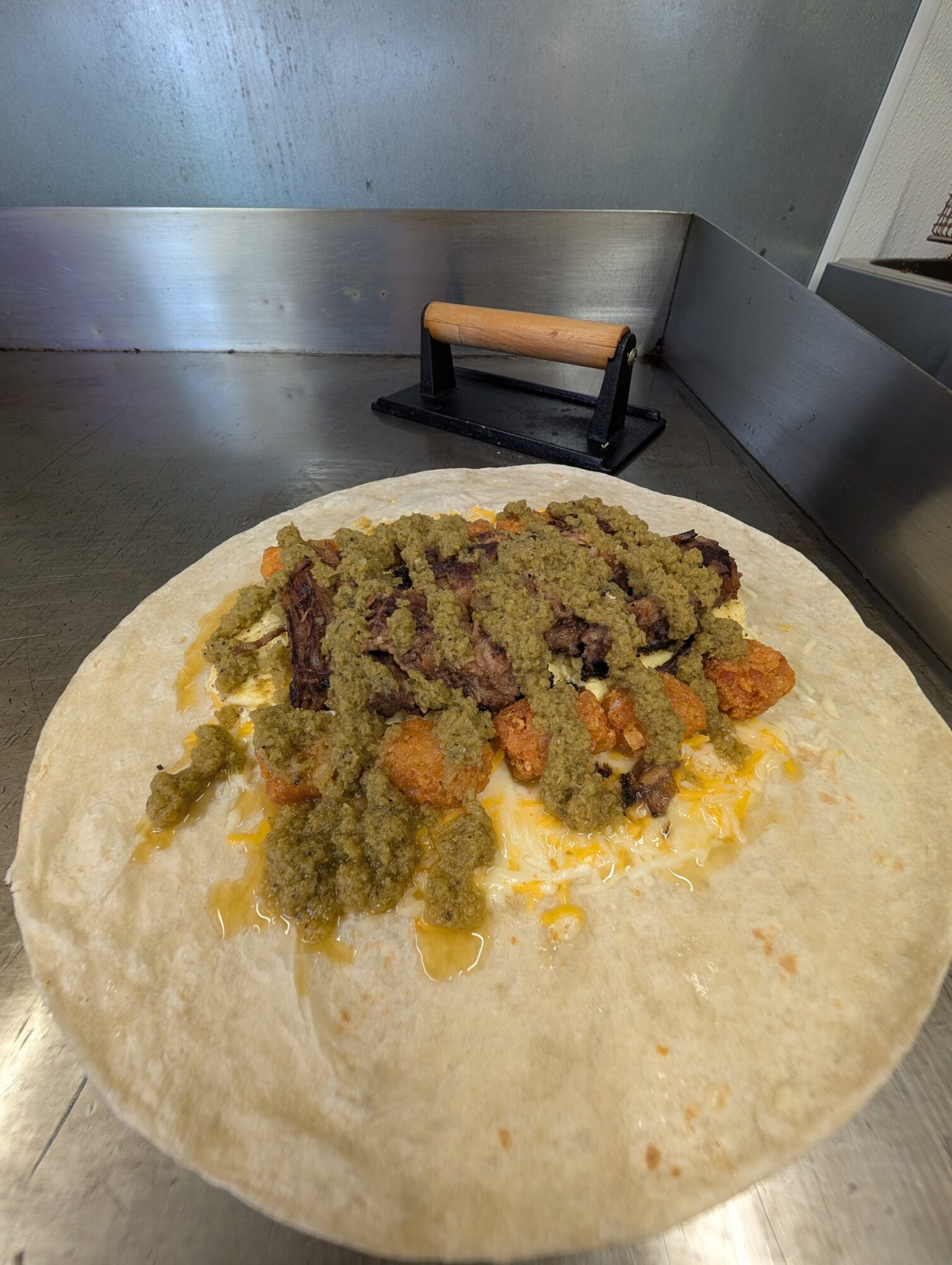 Unwrapped burrito with meat, vegetables, and sauce on a metal surface, with a pizza cutter in the background.