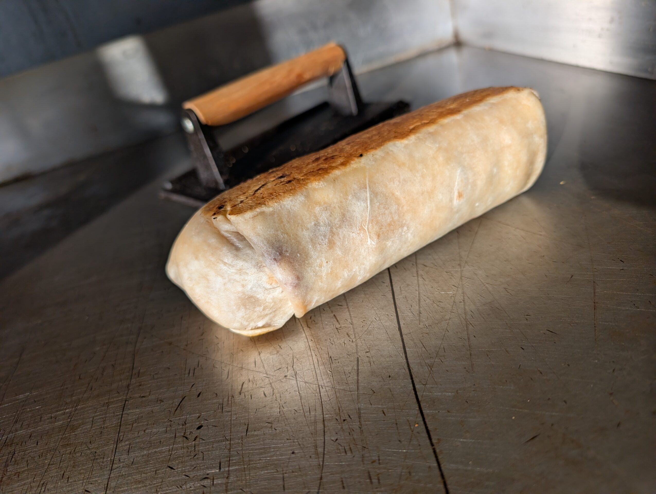 A loaf of bread on a metal surface with a handle in the background.