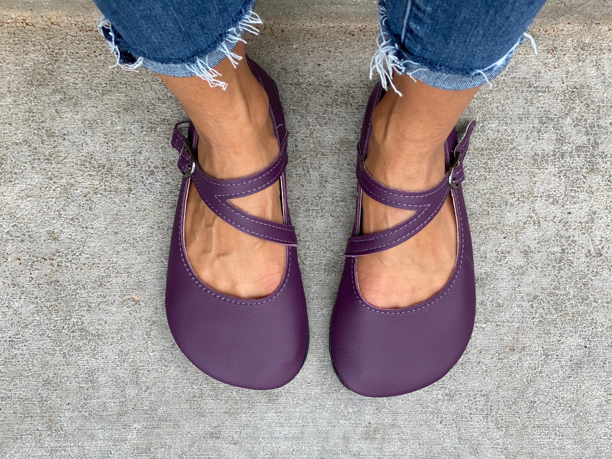 Person wearing purple shoes and ripped jeans standing on concrete surface.