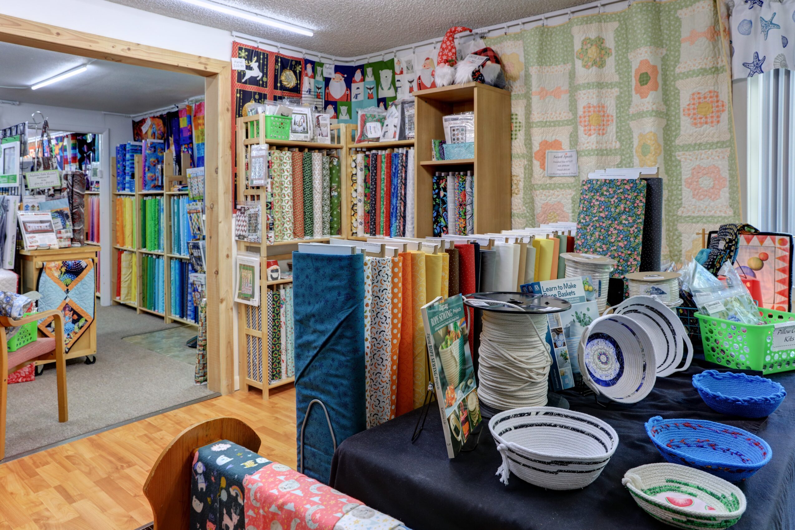 Room with shelves of fabric rolls, tables with bowls, and a wall with patterned wallpaper.