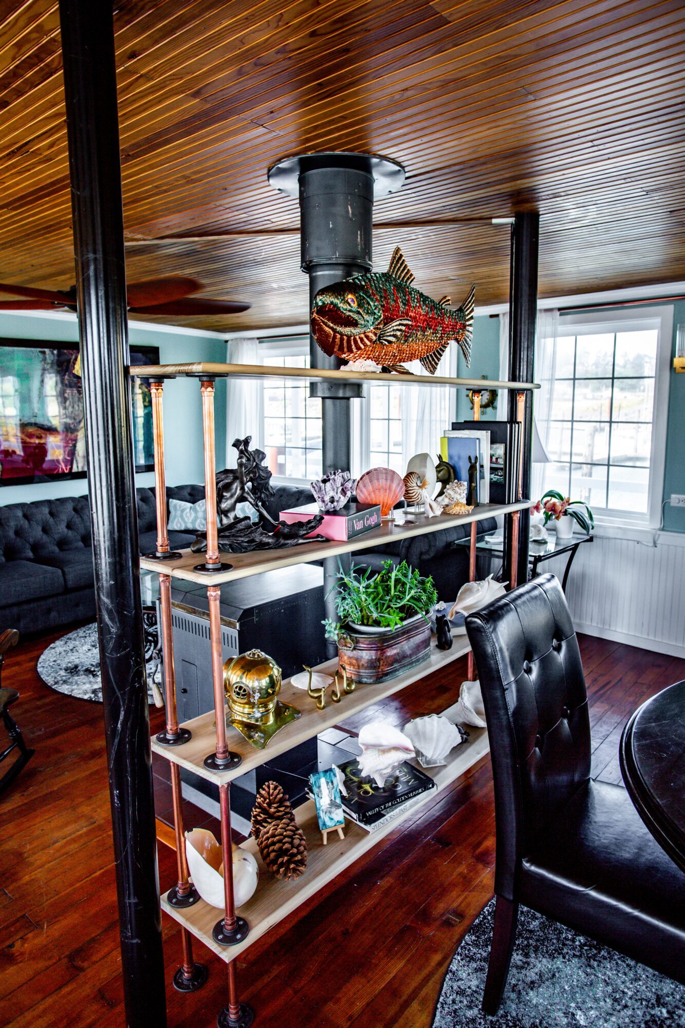 Shelving unit with decorative items, plants, and collectibles in a room with wooden ceiling and large windows.