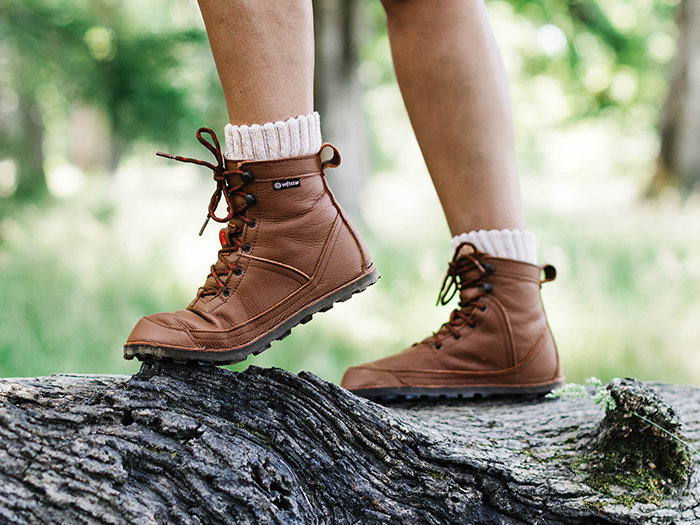 Person wearing brown hiking boots and white socks standing on a fallen tree trunk outdoors.
