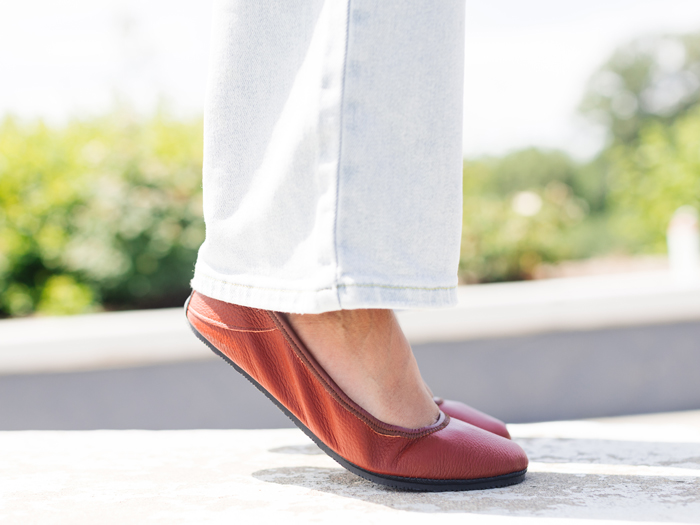 Close-up of a person wearing brown flats and light-colored pants standing outdoors on a sunny day.
