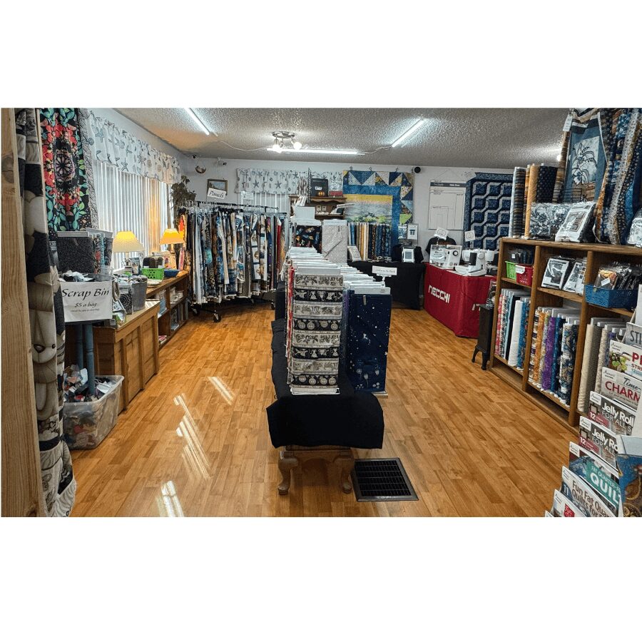 Interior of a fabric and quilting store with shelves of fabric, quilting supplies, and a display table in the center.