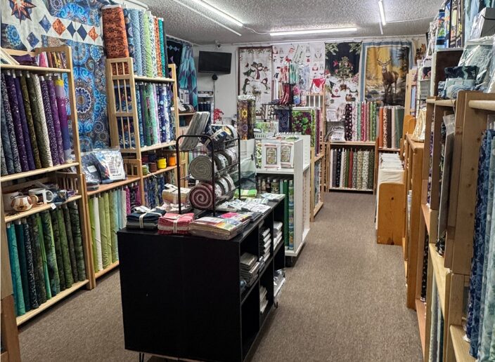 Interior of a fabric store with shelves filled with colorful fabric rolls, a central display table, and a mural on the back wall.