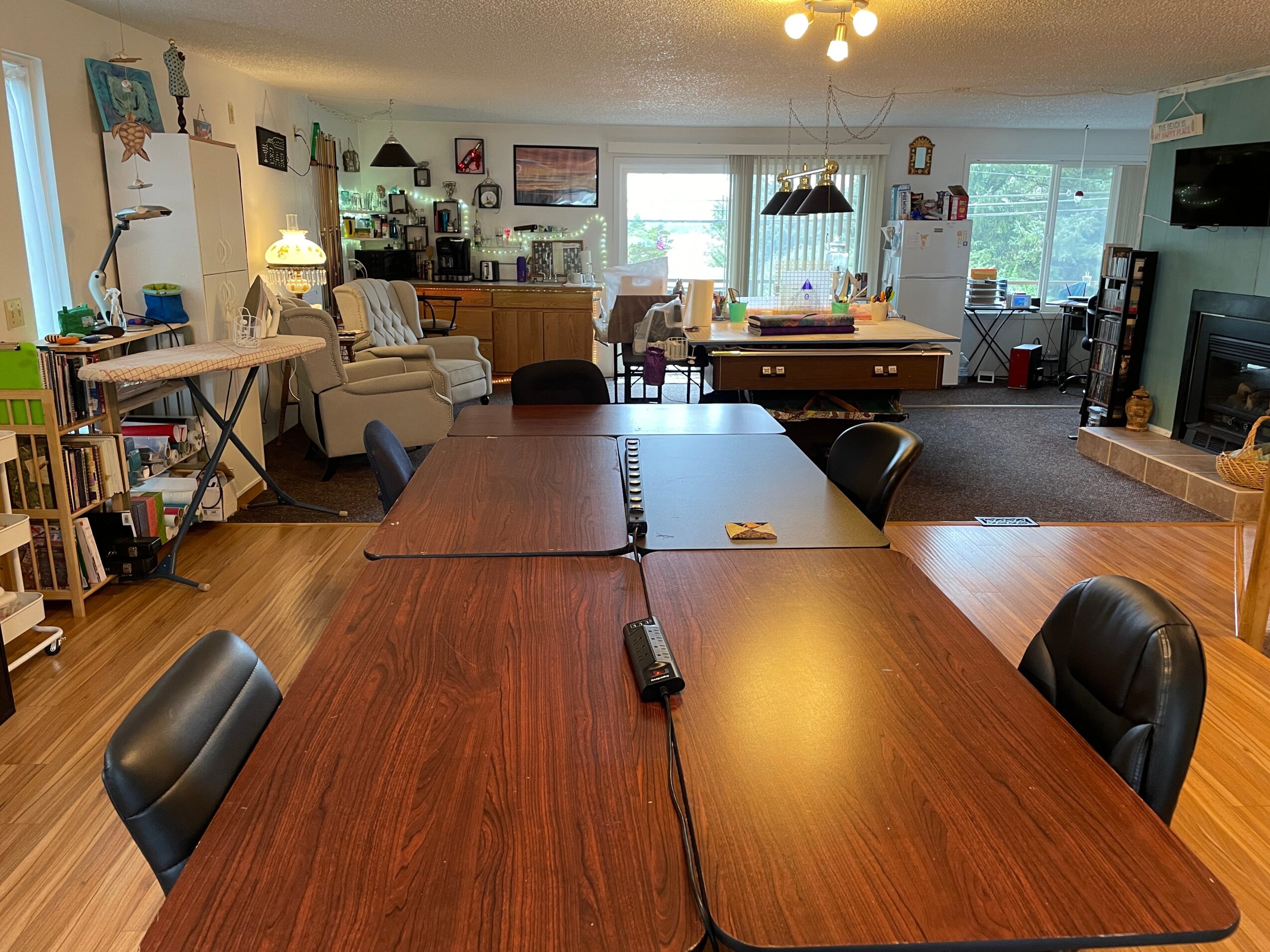 Living room with dining table, chairs, sofa, TV, and windows, viewed from the dining area, with natural light and wooden flooring.