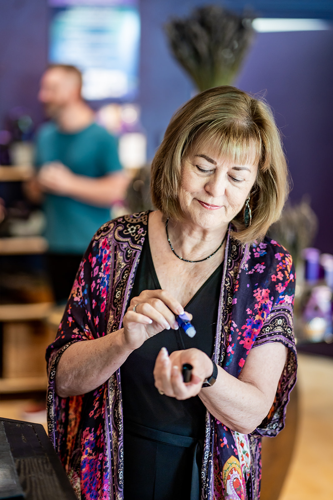 Woman with shoulder-length hair looking at her wristwatch in a room with blurred background of a person and screens