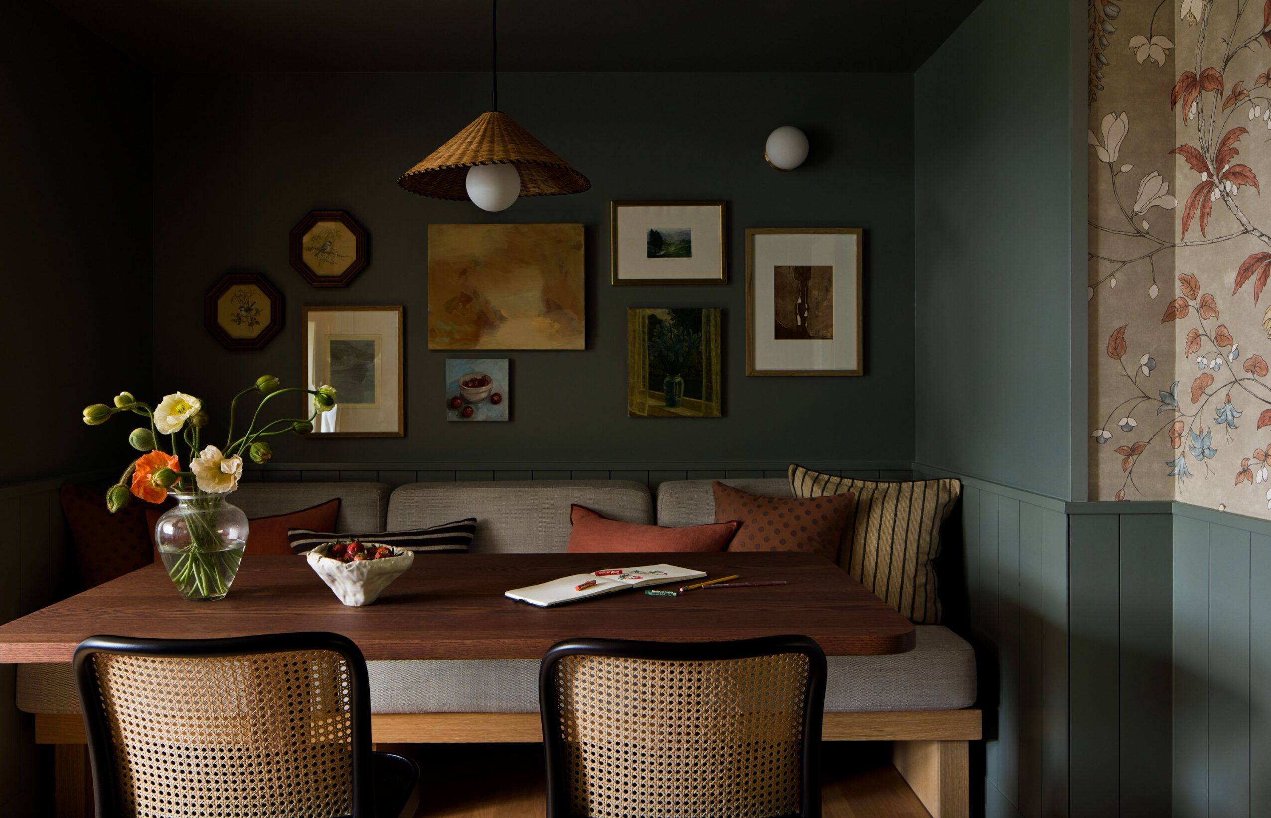 Dining area with a wooden table, chairs, a wall decorated with framed pictures, and a floral curtain on the right.