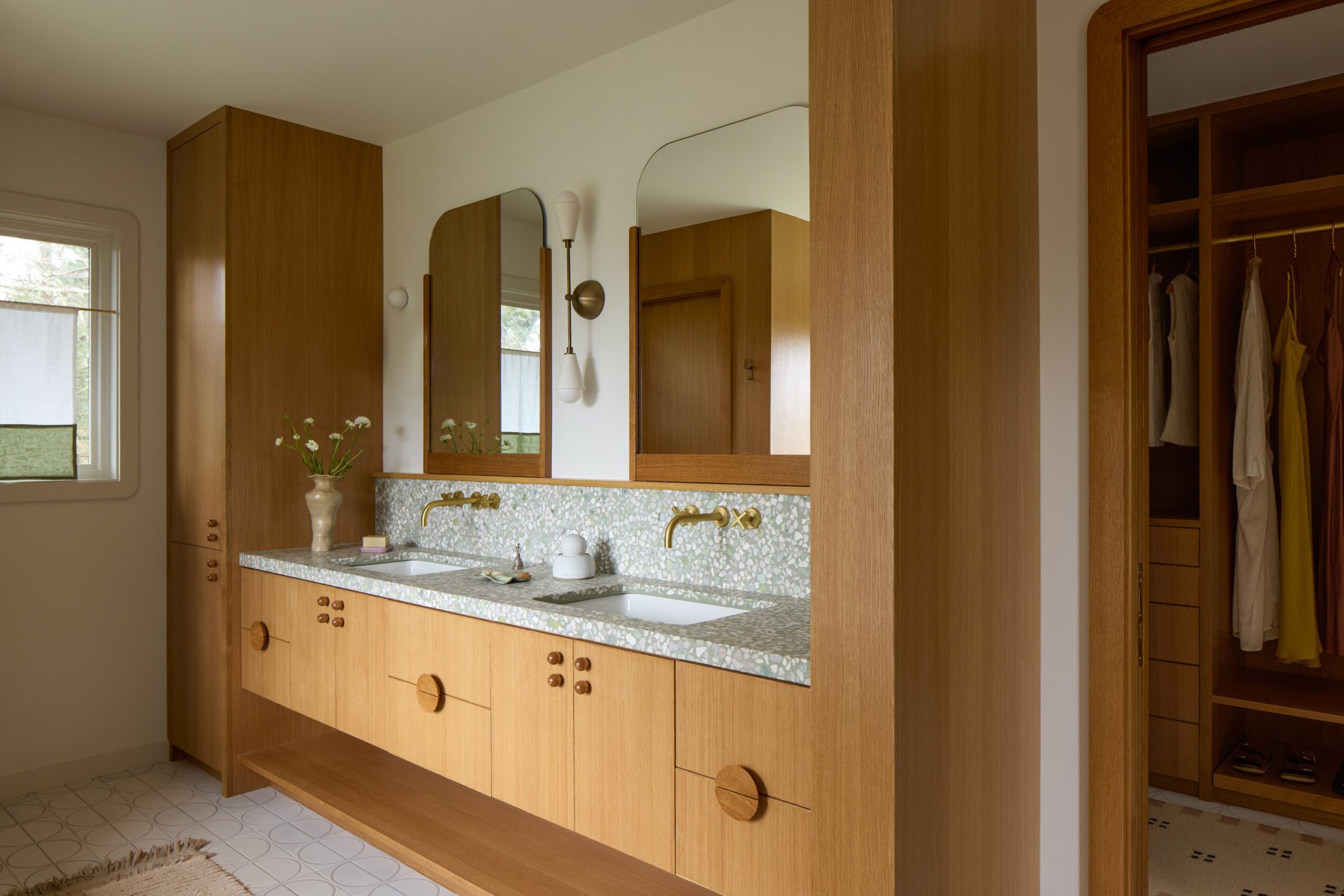 Bathroom with wooden cabinets, a granite countertop, two mirrors, and a window, with an open closet visible on the right.