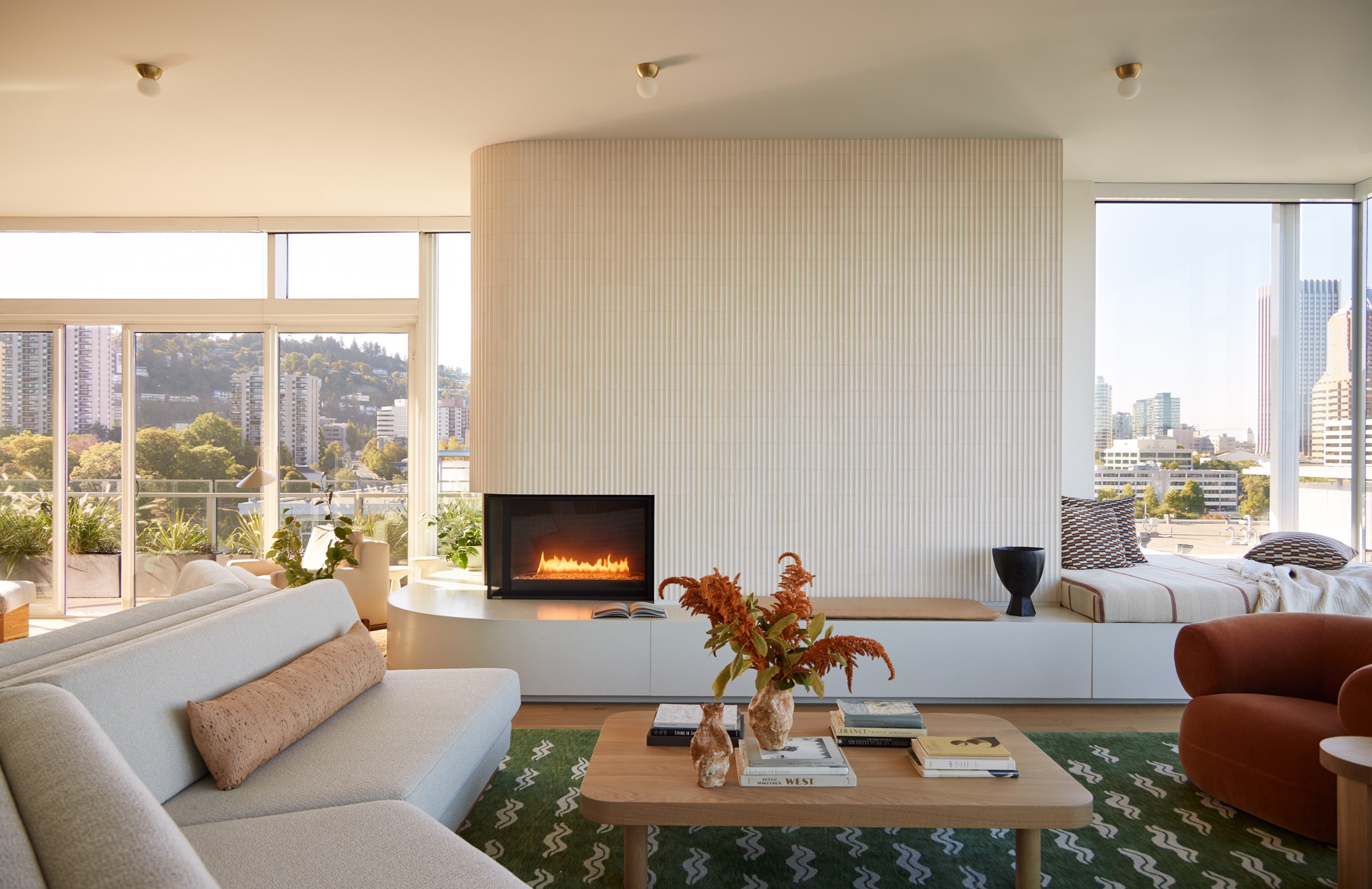 Living room with a fireplace, white sofa, coffee table, and city view through large windows.