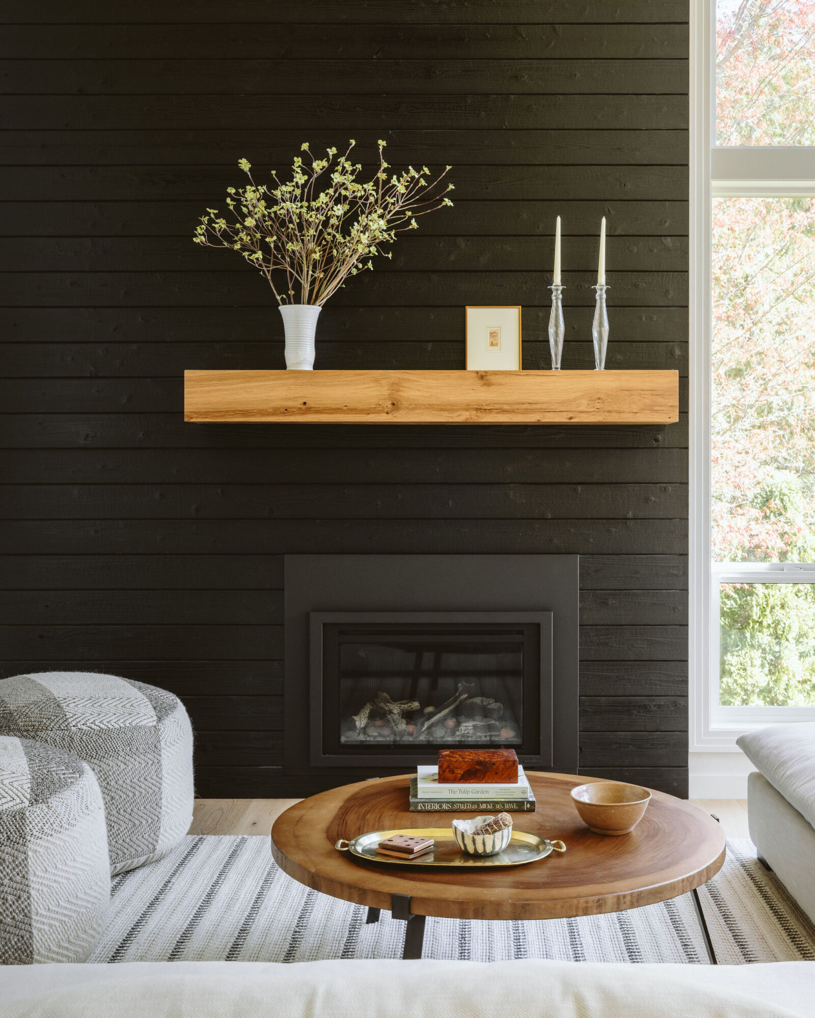 Living room with a black wall, wooden shelf with decorative items, fireplace, and a round coffee table with books and bowls.
