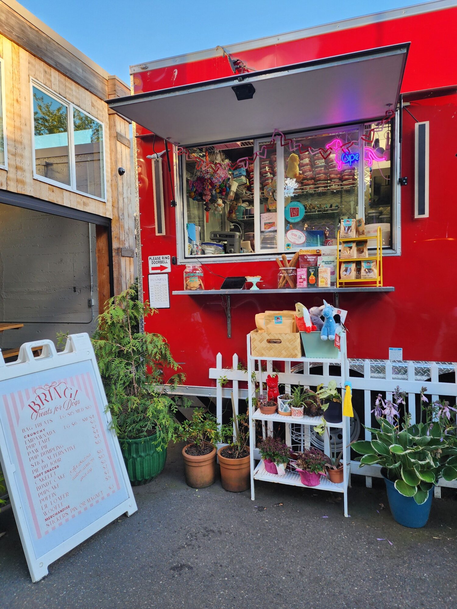 Red storefront with display window, potted plants, and a white menu board outside, on a sidewalk.