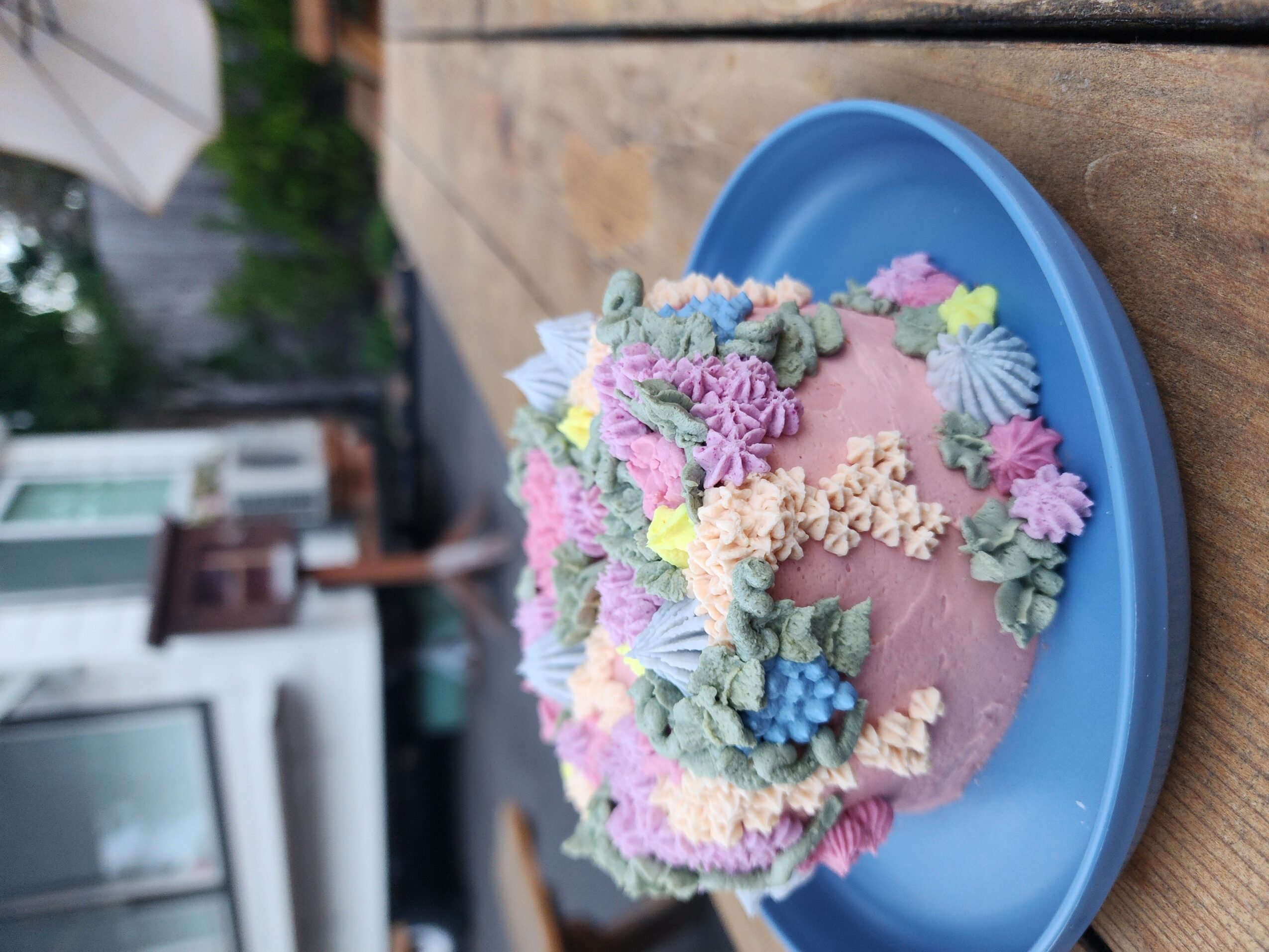 A decorated cake with pastel-colored frosting and floral decorations on a blue plate, placed on a wooden surface.