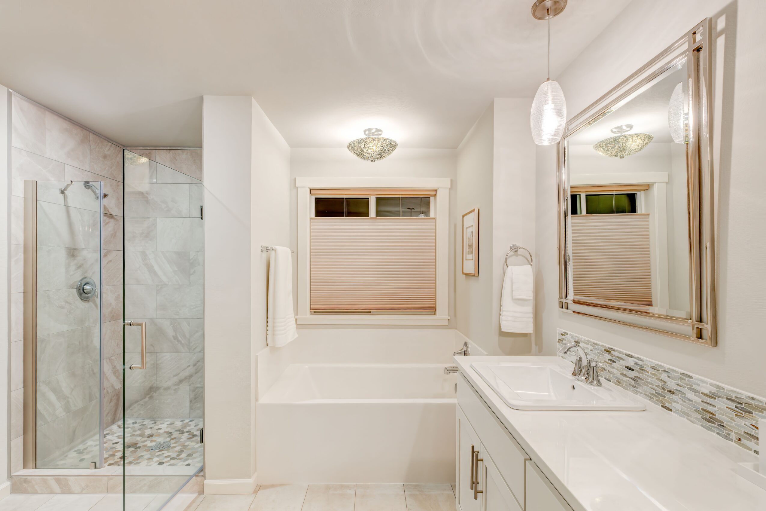 Bathroom with shower, window, mirror, and vanity with sink, towels, and lighting fixtures, bright and clean space.