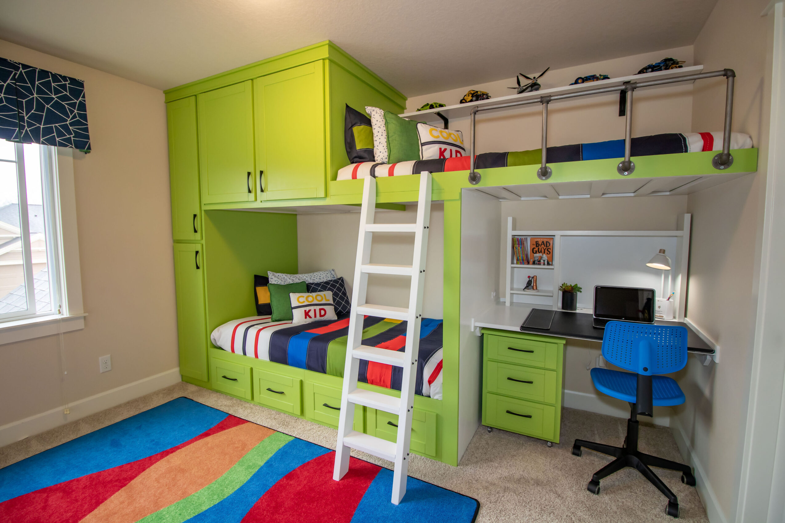 Children's bedroom with green furniture, bunk bed, desk, blue chair, window, and colorful rug.