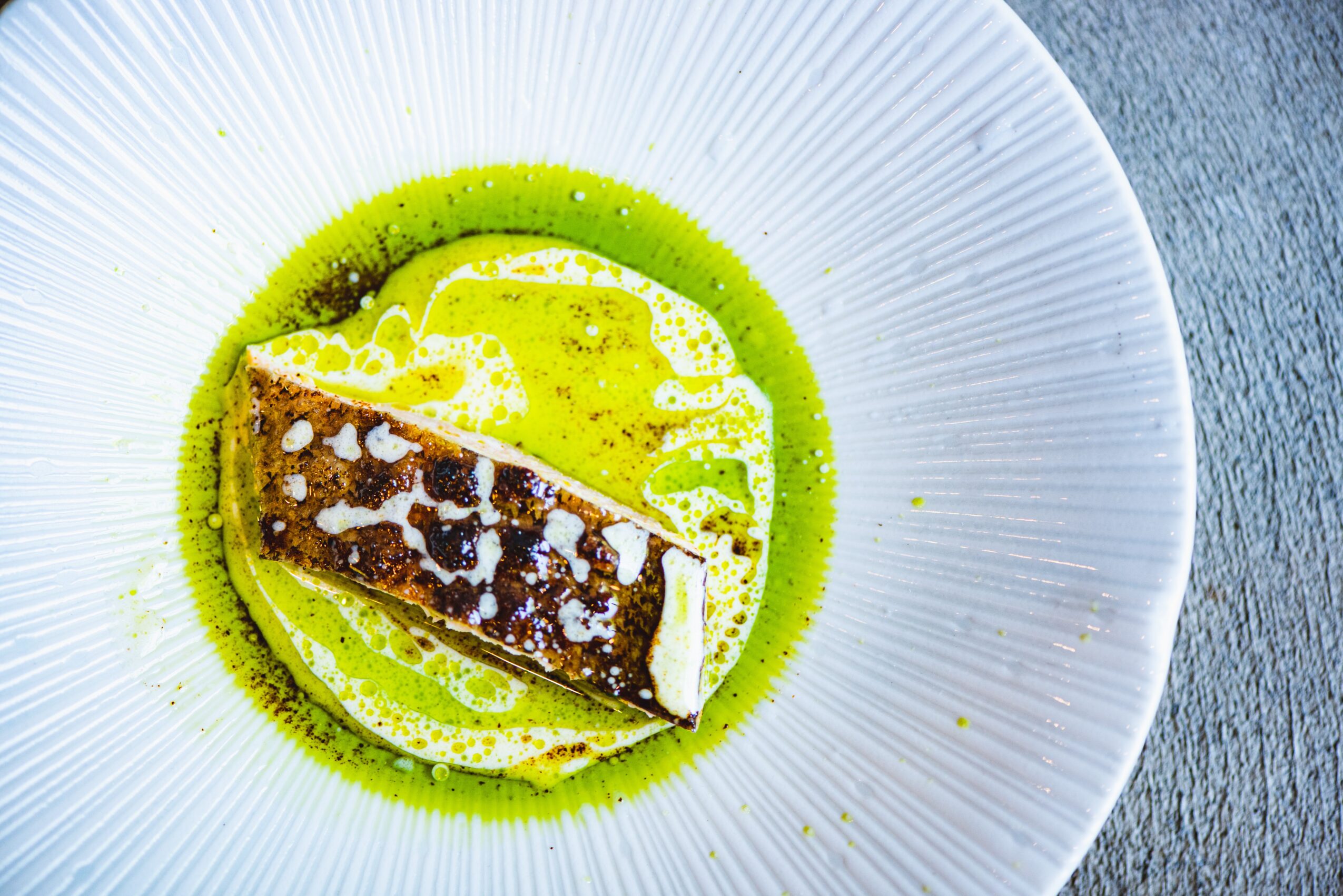 A dessert with a rectangular piece of cake on a green sauce, served on a white plate, viewed from above.