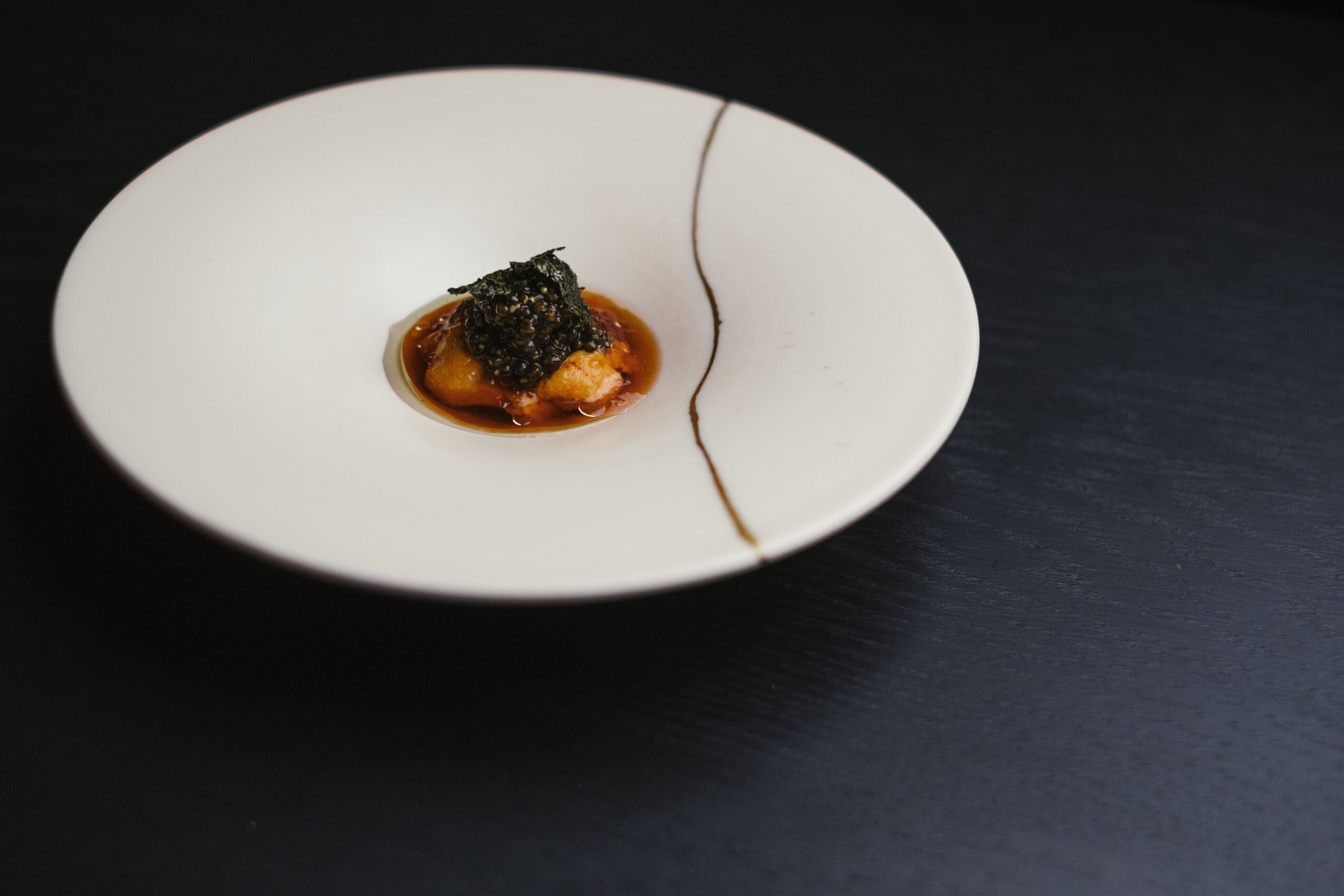 Empty white plate with a small portion of food and sauce, on a dark surface.