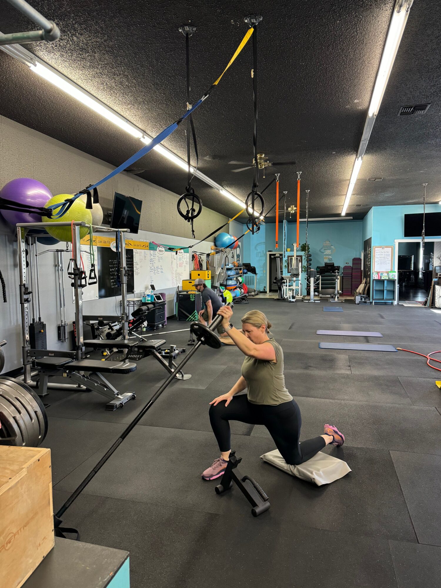 Person performing a yoga pose on a mat in a gym with workout equipment and a purple exercise ball.