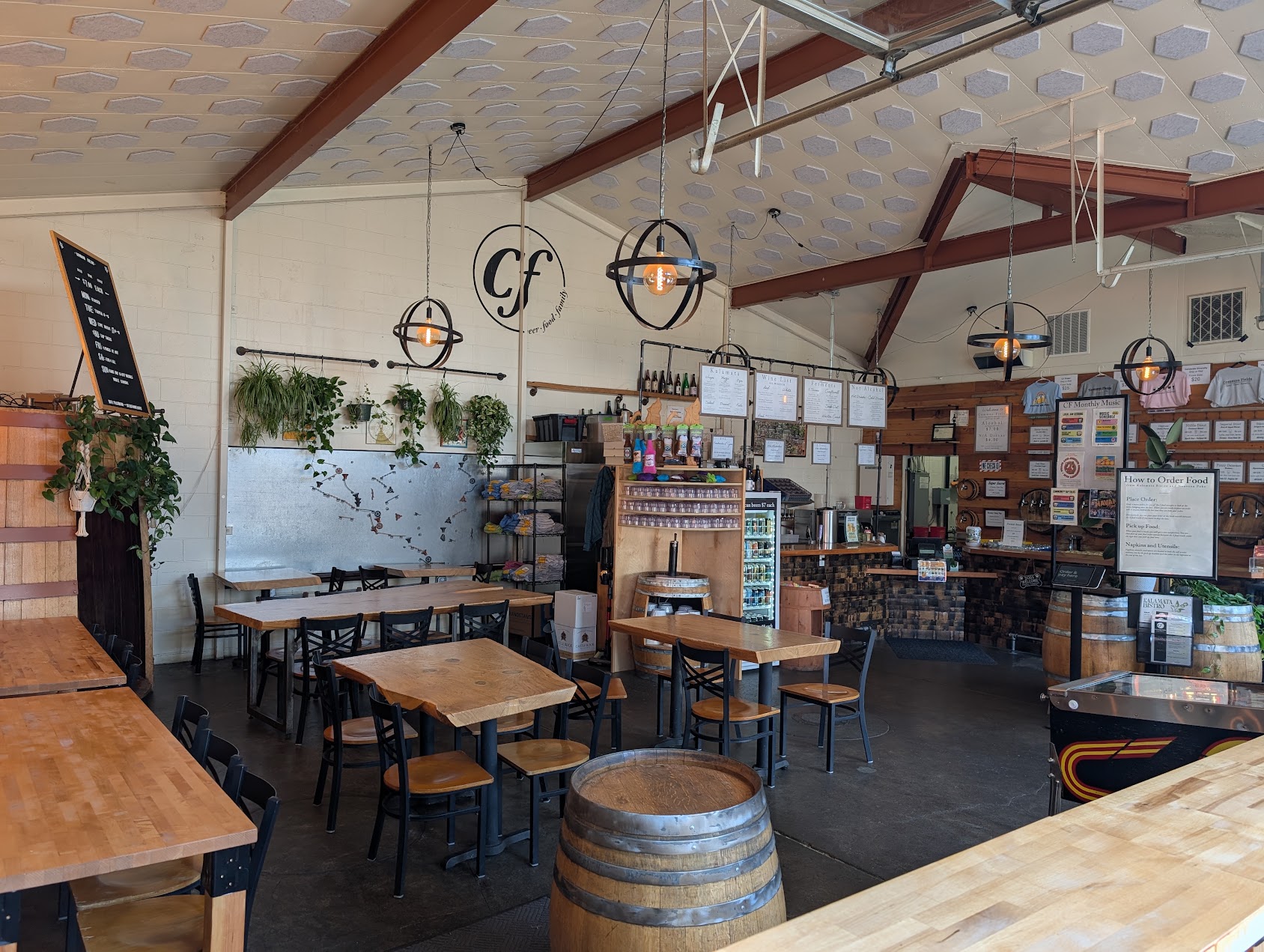 Interior of a cafe with wooden tables, chairs, and decorative hanging lights, plants on the wall, and a counter area.