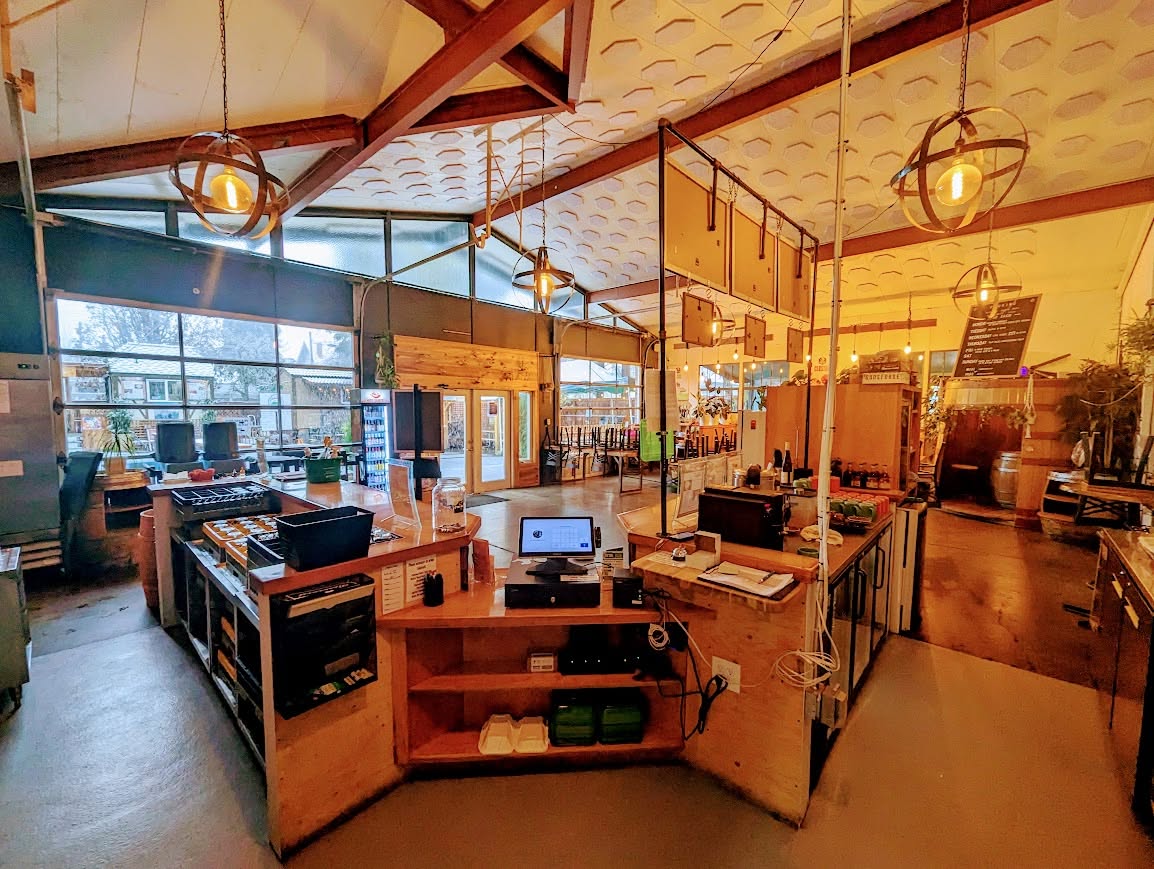 Interior of a modern cafe with tables, chairs, and large windows, illuminated by hanging pendant lights and natural light.