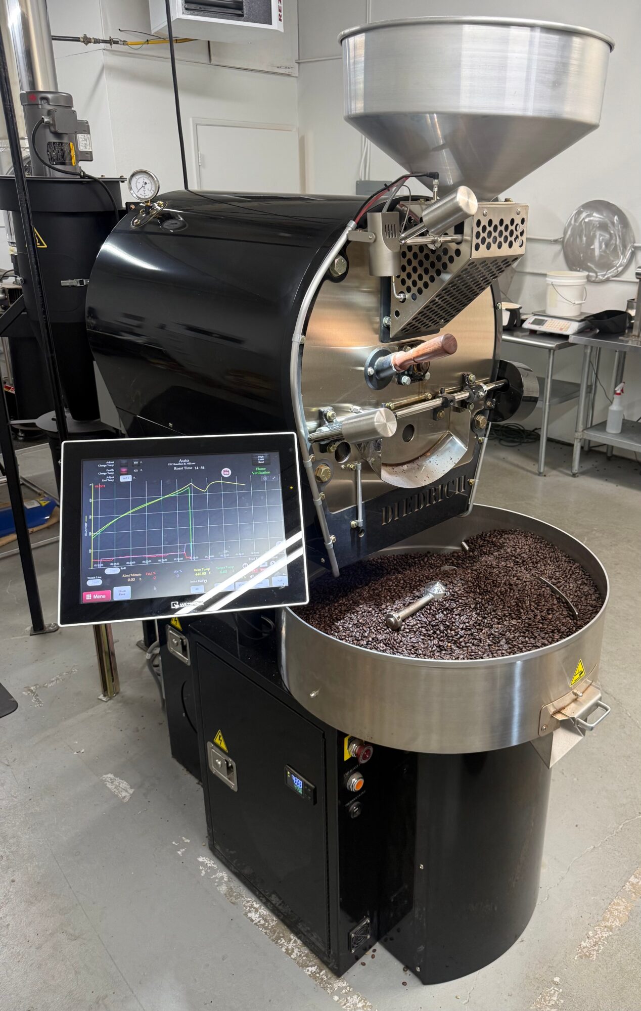 Coffee roasting machine with a digital control panel and a large drum, in a commercial kitchen setting.