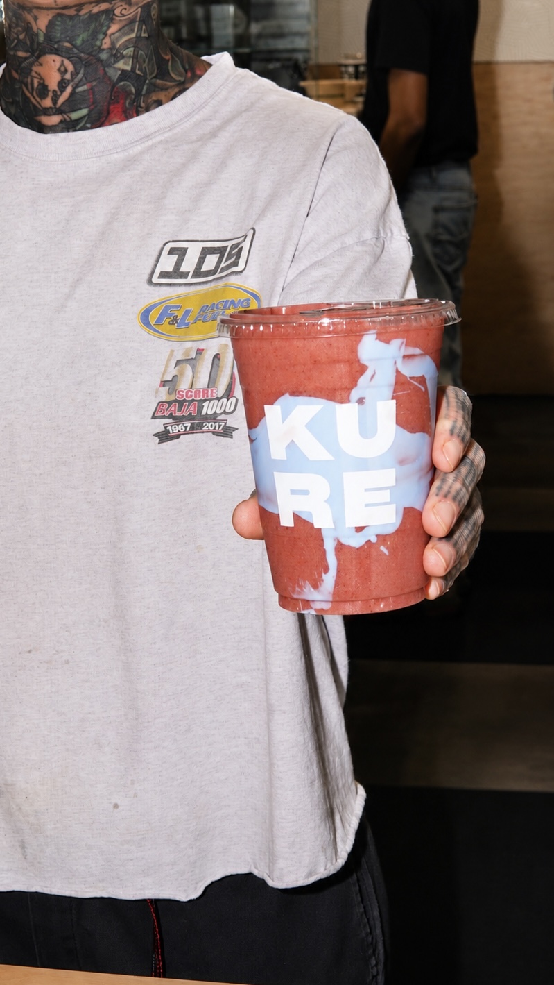 Person holding a red cup with white and blue text, wearing a gray T-shirt with a graphic design, in a casual setting.