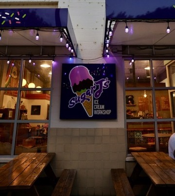 Exterior of a shop with a sign for Sugar's Ice Cream Workshop, featuring an ice cream cone graphic, at night.
