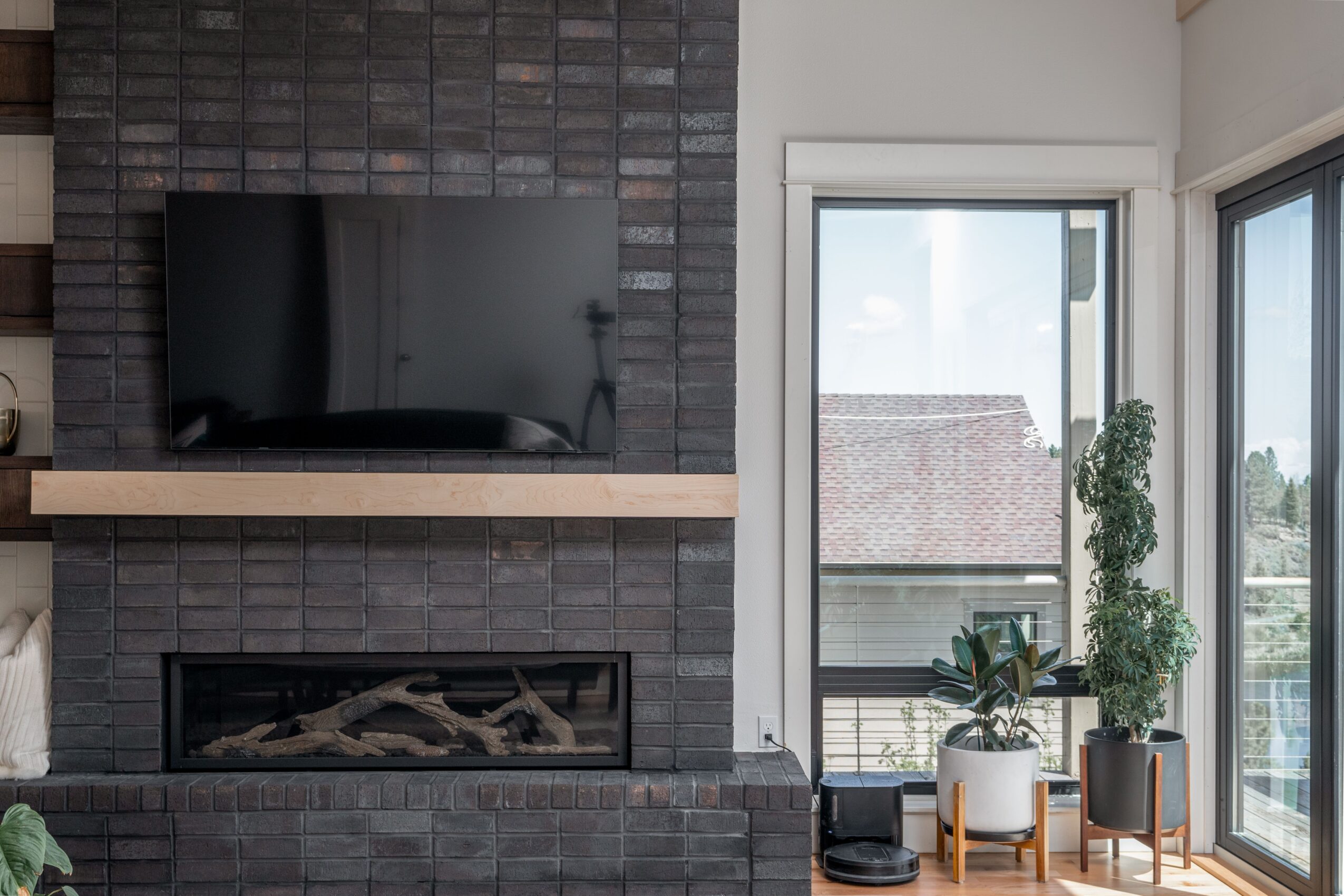 Living room with a wall-mounted TV above a fireplace, and a sliding glass door with plants outside.