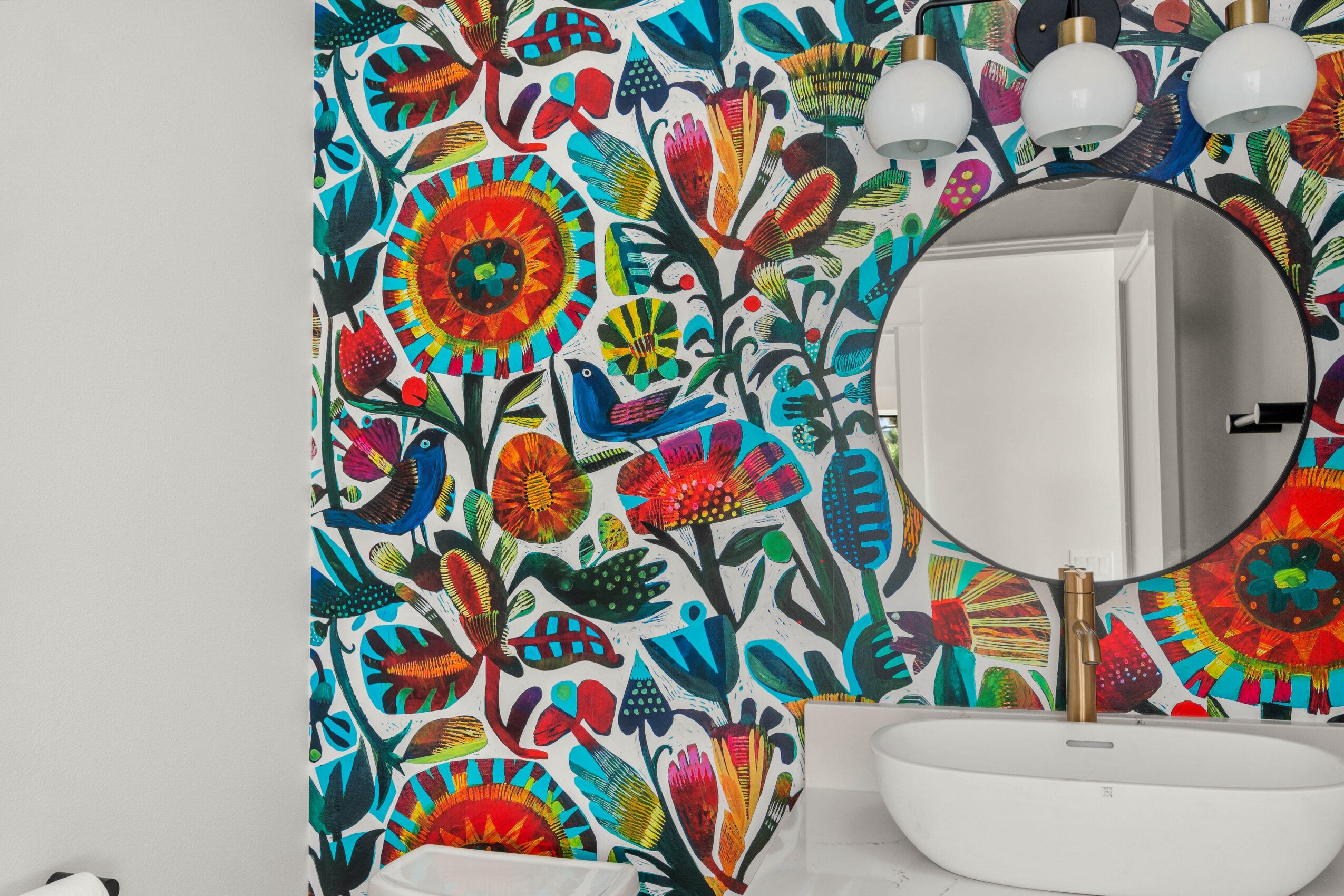 Decorative wall with colorful floral and butterfly pattern, round mirror, and white vessel sink.