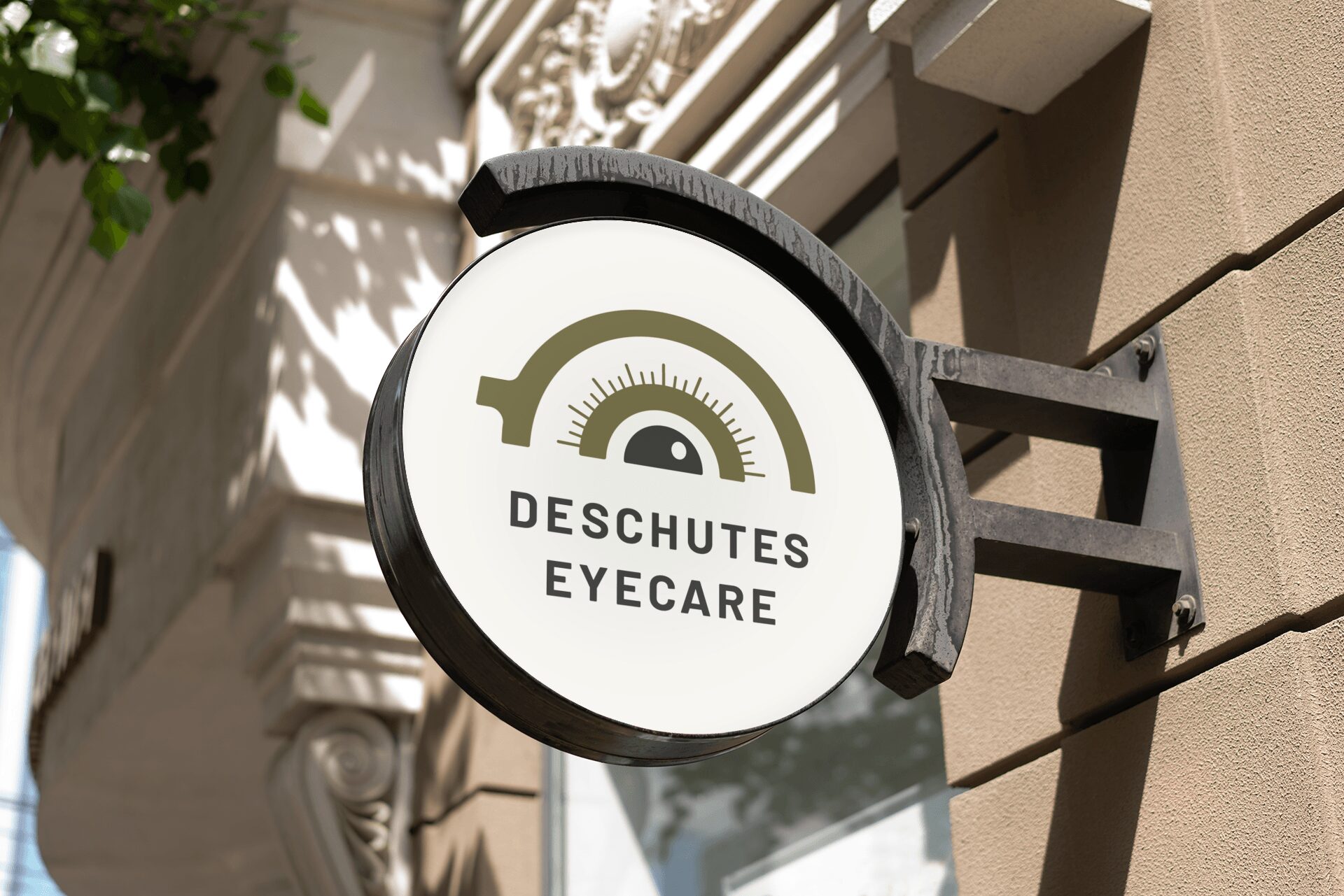 Round sign for Deschutes Eyecare with a gauge graphic, mounted on a building exterior, with architectural details and shadows.