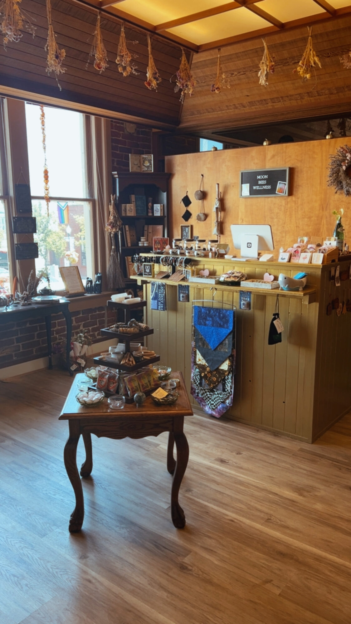 Interior of a cozy shop with wooden walls, a counter, and a small table displaying items, sunlight streaming through windows.